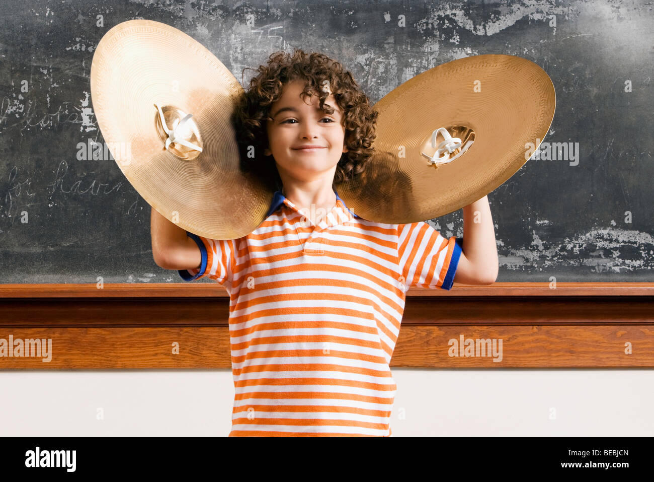 Schoolboy playing cymbals in a classroom Stock Photo, Royalty Free