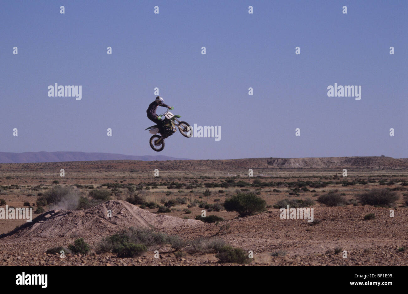 Trail bike motorbike rider jumps a hill in the desert outback Stockfoto