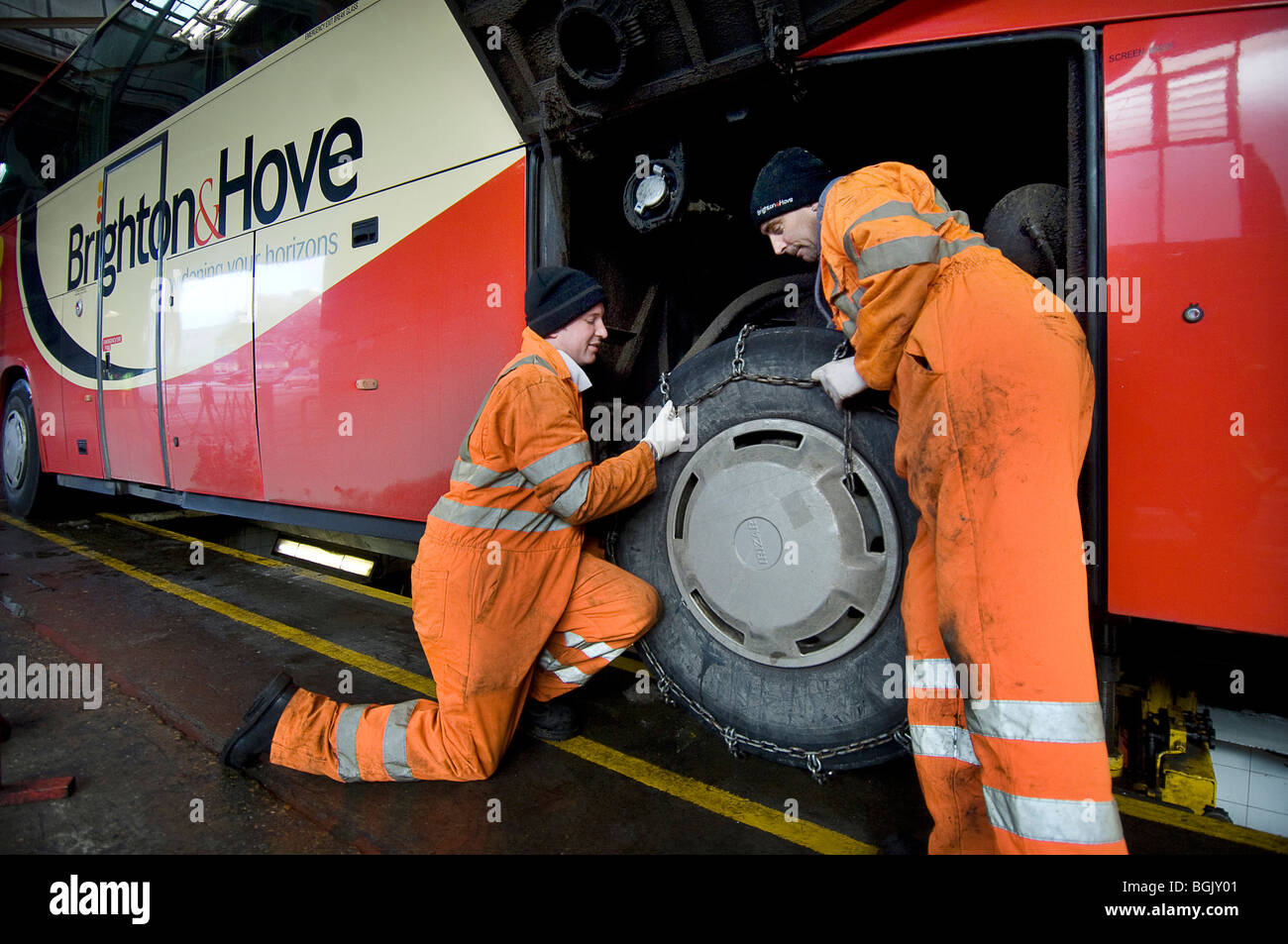 Two mechanics fitting snow chains to a bus wheel using a bus garage Stock Photo, Royalty Free