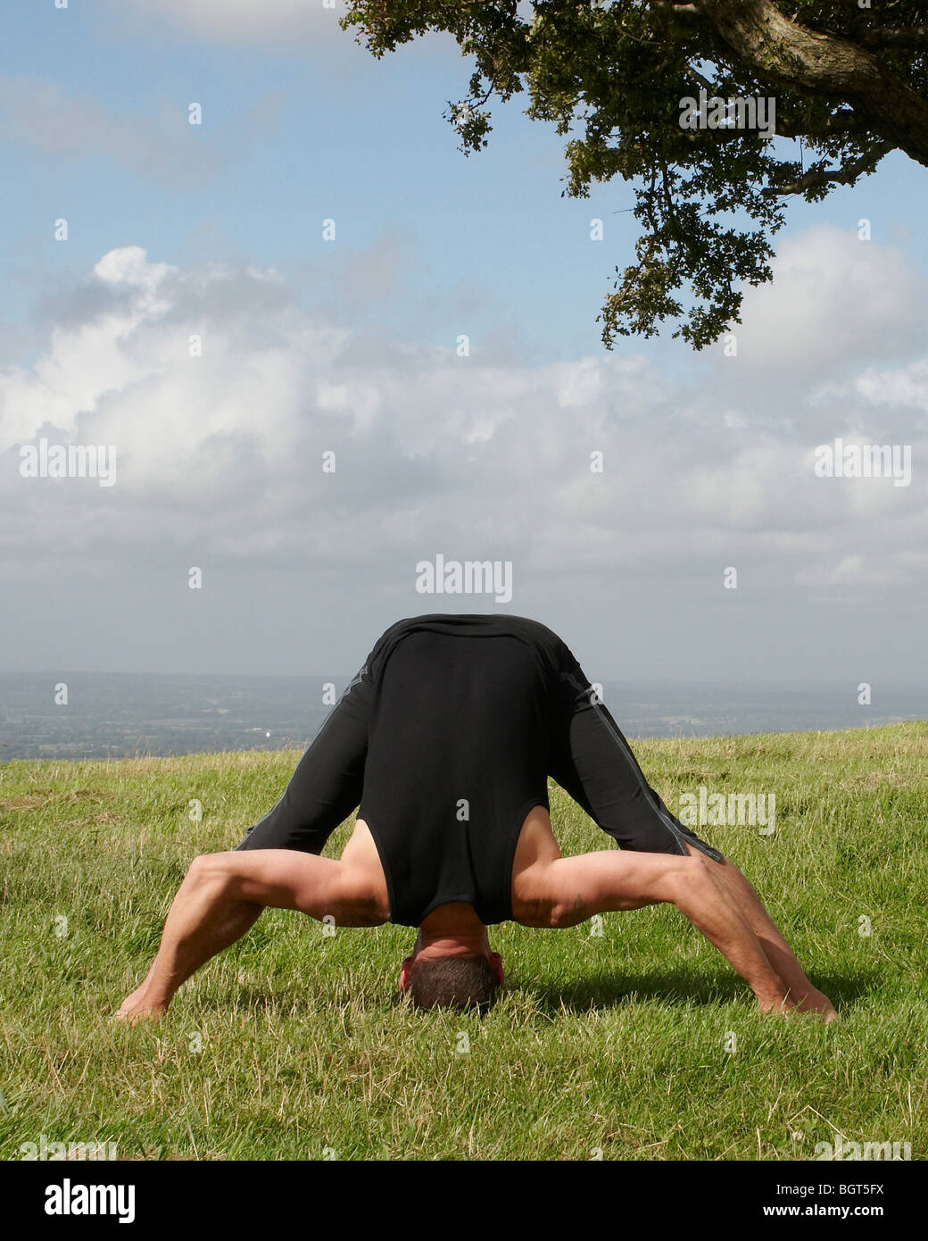 Man Doing Yoga On Hillside With View Of English Countryside Behind
