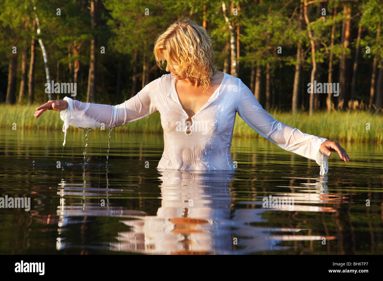 Woman swimming in dark forest lake, nice reflection from water Stock