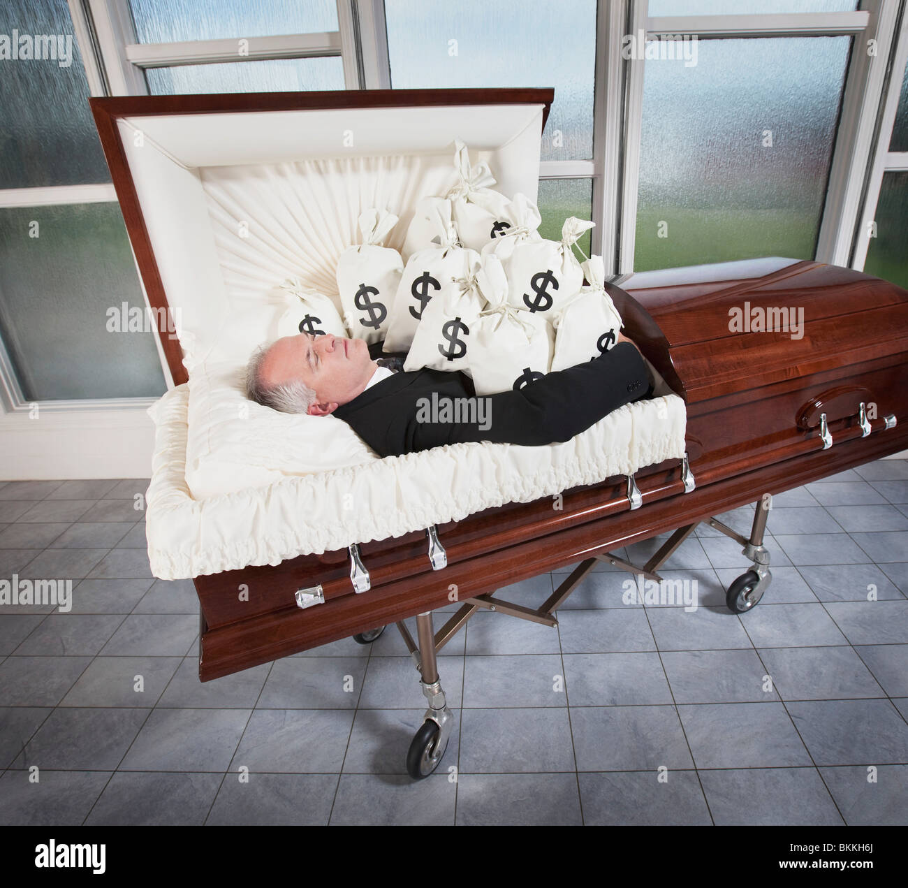 a-man-laying-in-a-coffin-surrounded-by-bags-of-money-BKKH6J.jpg