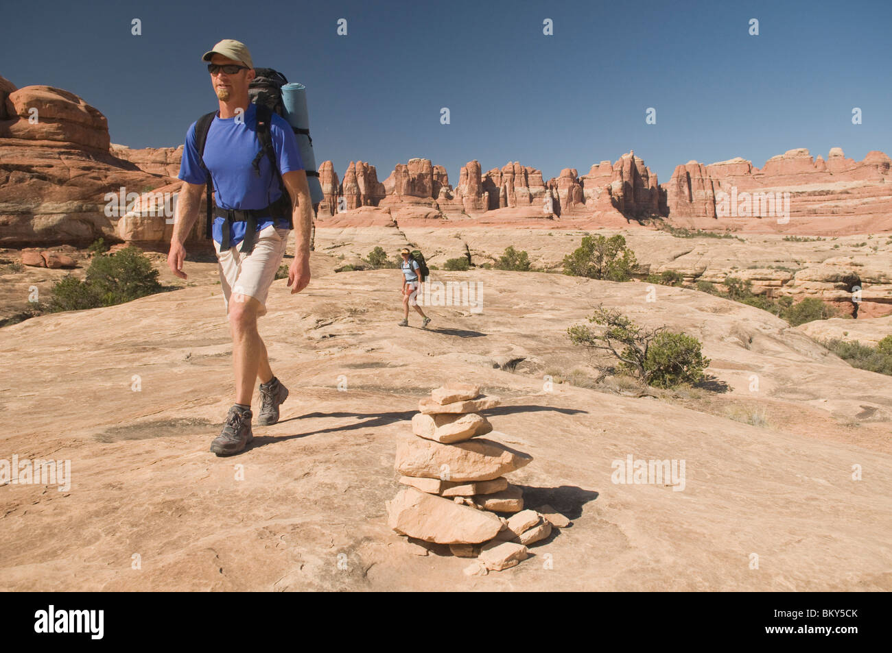 http://c8.alamy.com/comp/BKY5CK/man-and-woman-hiking-along-a-sandstone-trail-marked-with-cairns-canyonlands-BKY5CK.jpg