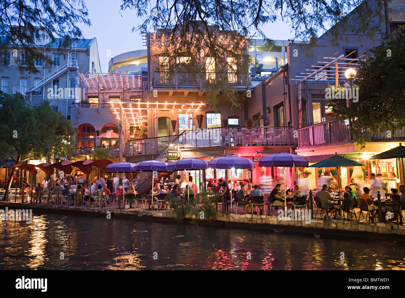 People eating at tables in shade at dusk on San Antonio River Walk