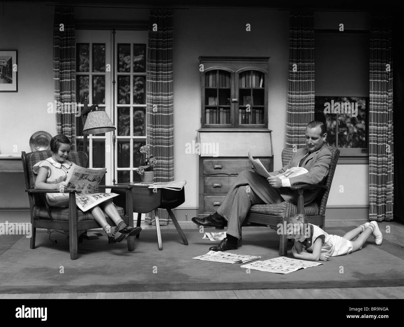 Living Room 1930s 1930s man father reading newspaper boy girl reading comics in Living Room 1930s 1930s man father reading newspaper boy girl reading comics in