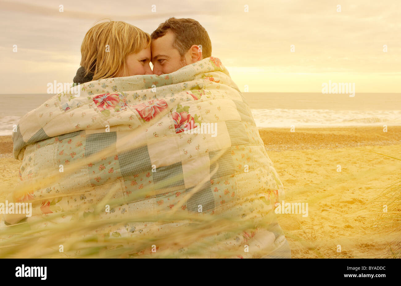 Couple cuddling under blanket on beach Stock Photo, Royalty Free Image
