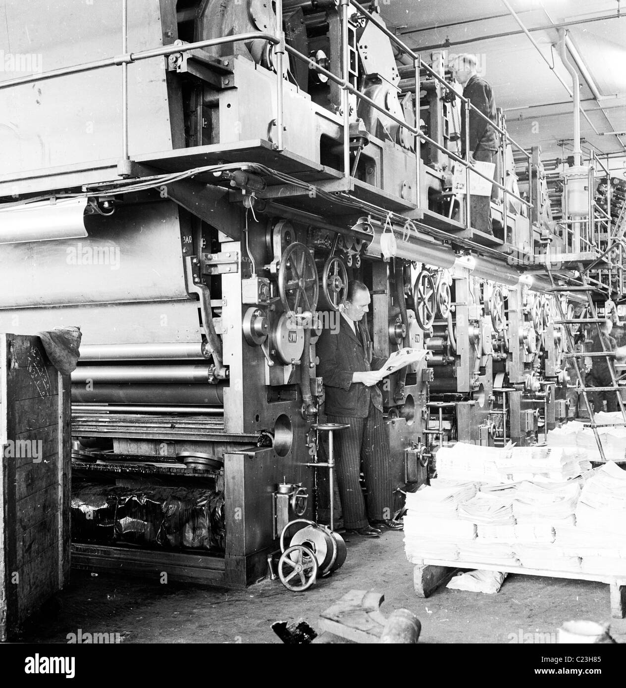 1950s. England. Worker stand by a large bank of printing presses in