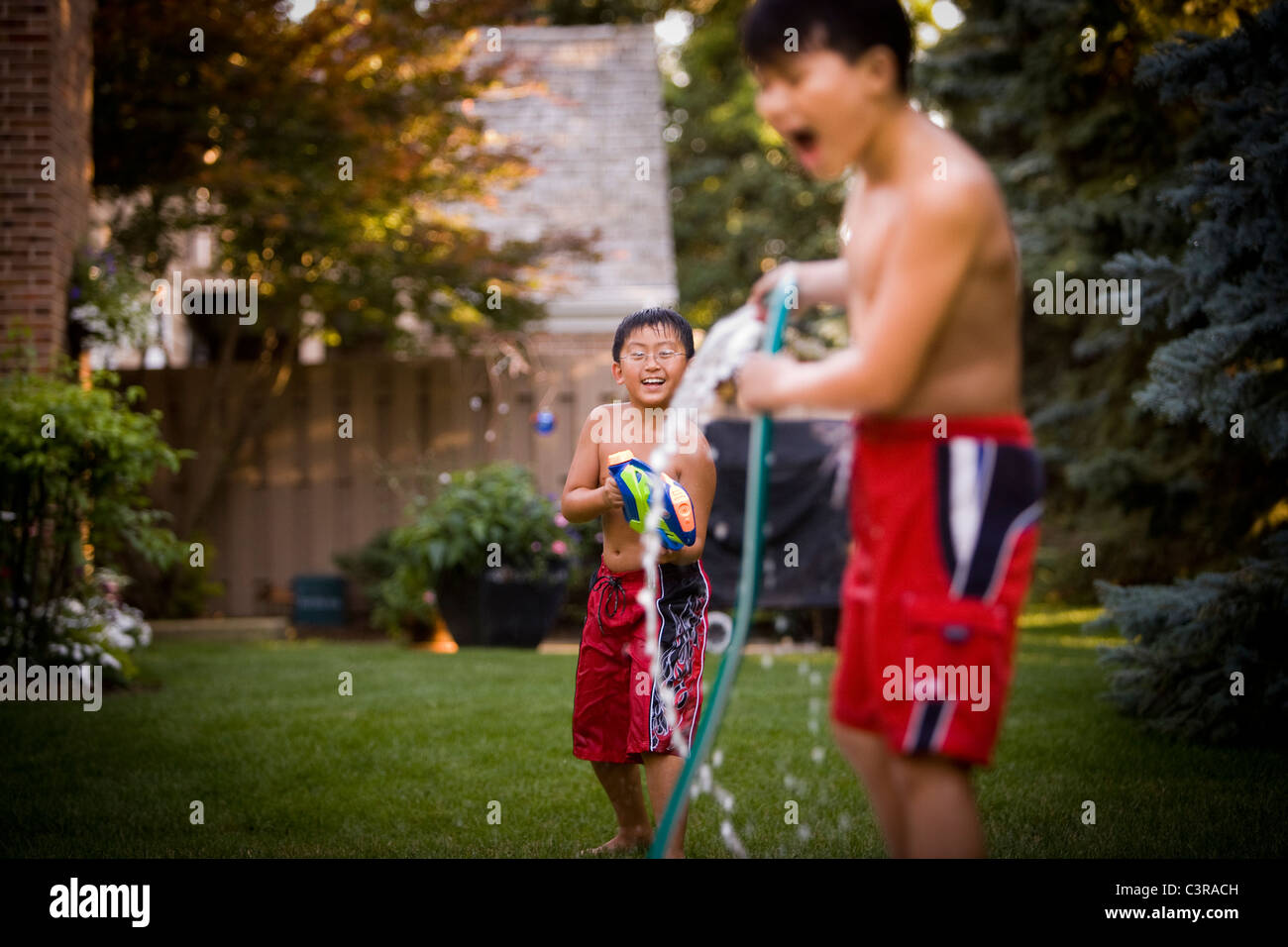 Young Boys Having A Water Fight In The Backyard Stock Photo