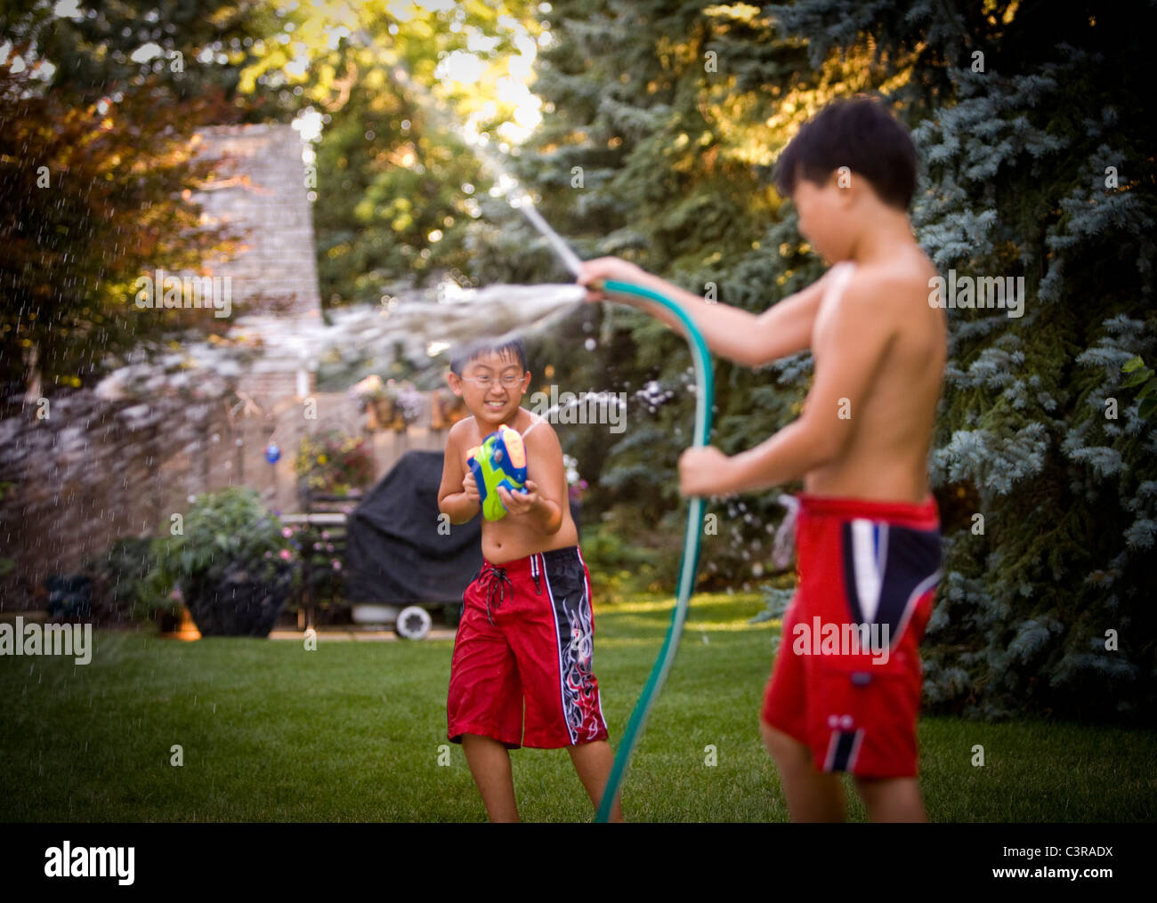 Young Boys Having A Water Fight In The Backyard Stock Photo