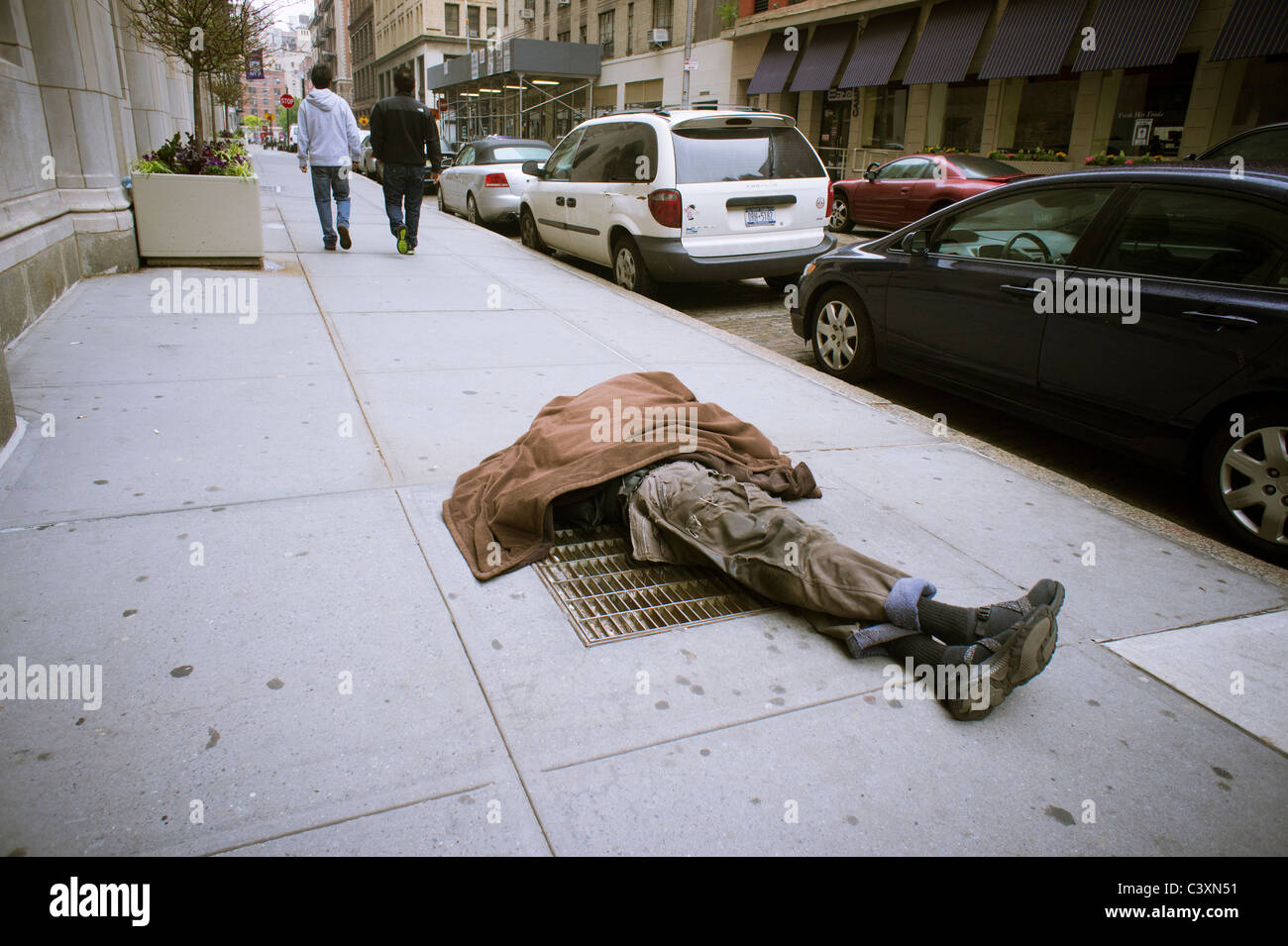 Homeless man sleeping on a vent in the sidewalk in Greenwich Village