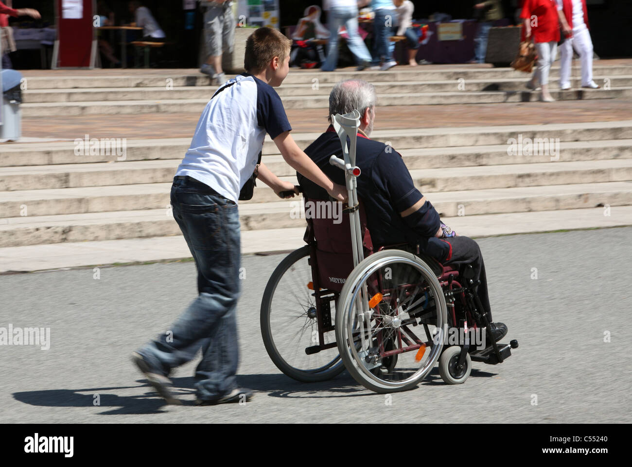Old man in a wheelchair pushed by a boy, Berlin, Germany Stock Photo