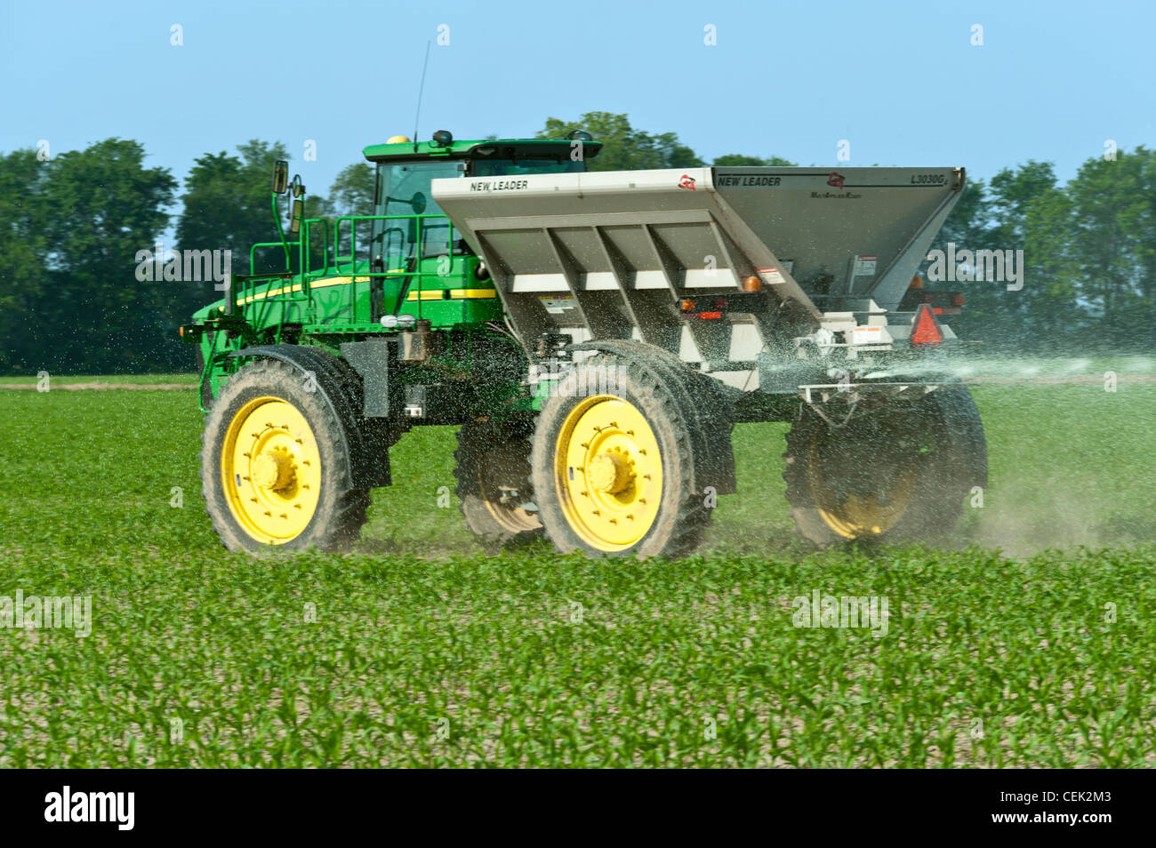 A John Deere HiBoy with a spin spreader box applies dry pelleted Stock