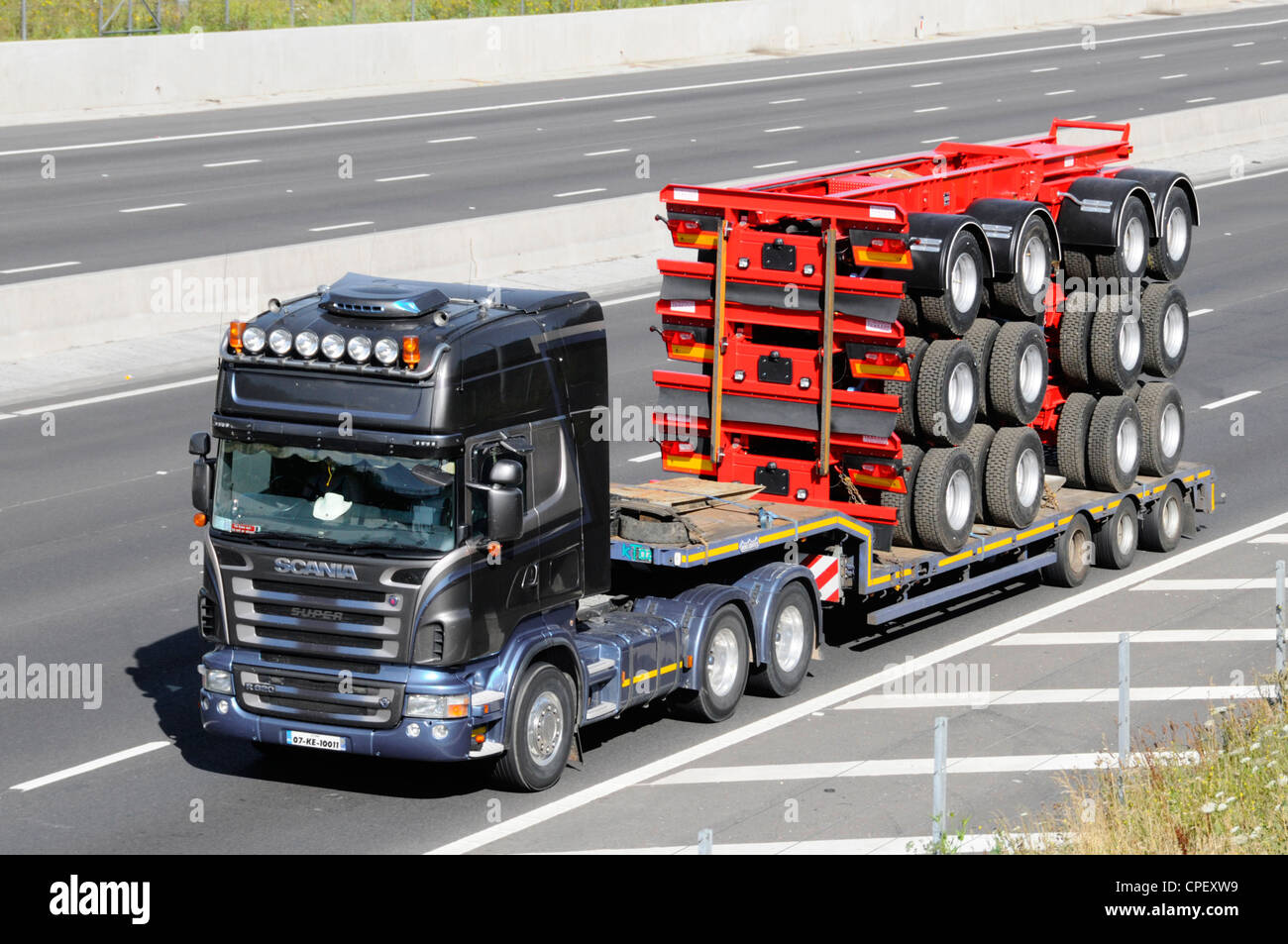 Black Lorry Towing Low Loader Trailer Carrying A Stack Of Truck Stock