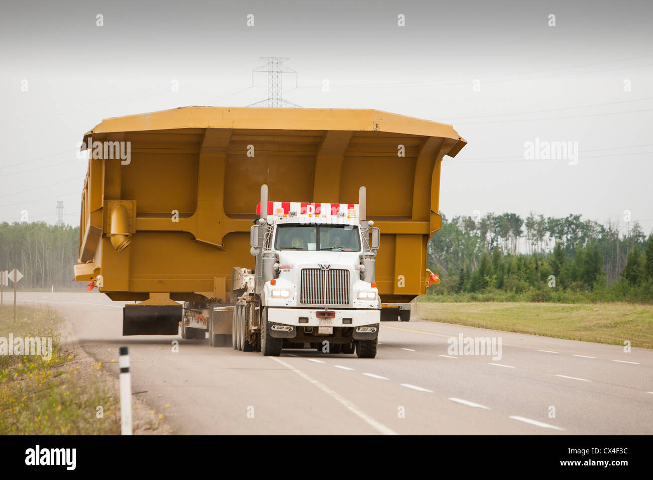 Trucks haul an oversize load, a massive dump truck used in the tar