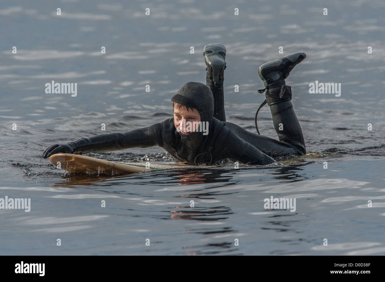 A young boy in black wetsuit paddles into the cold waters of the Stock