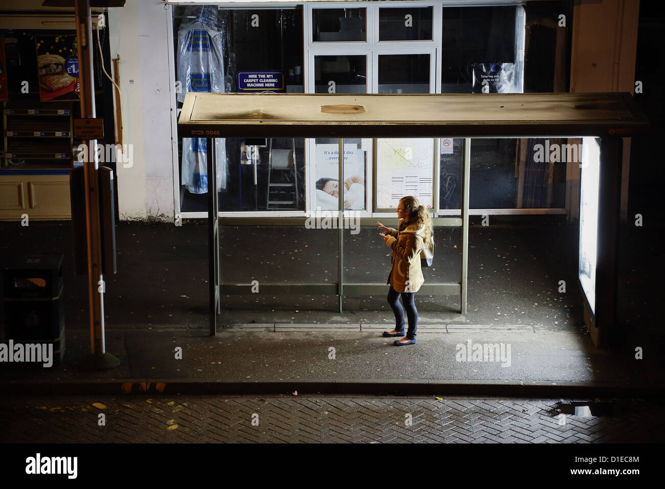 A young woman waiting alone at a bus stop at night in London UK Stock