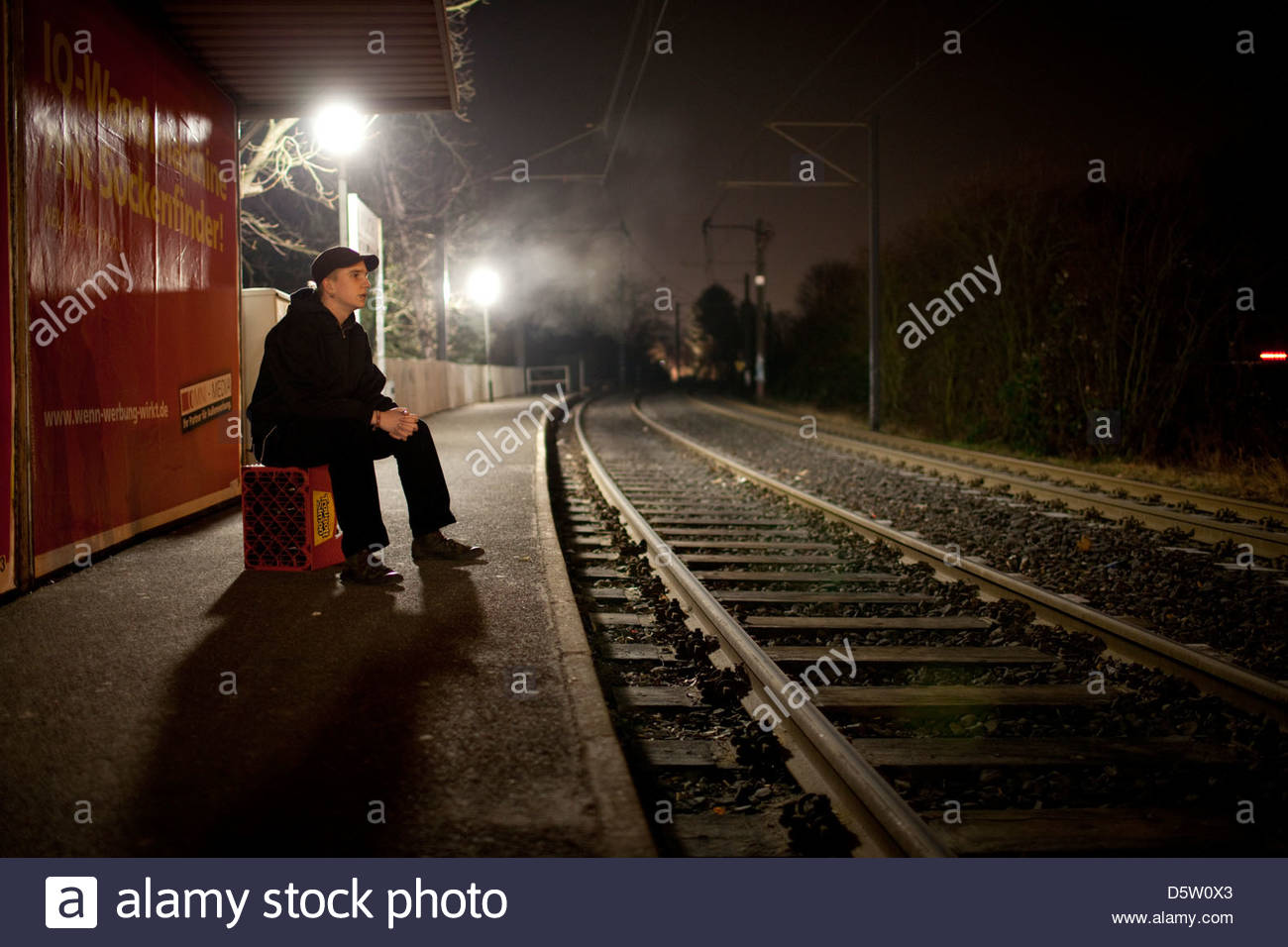 young man sitting on a crate waiting for a tram at night sitting jobs