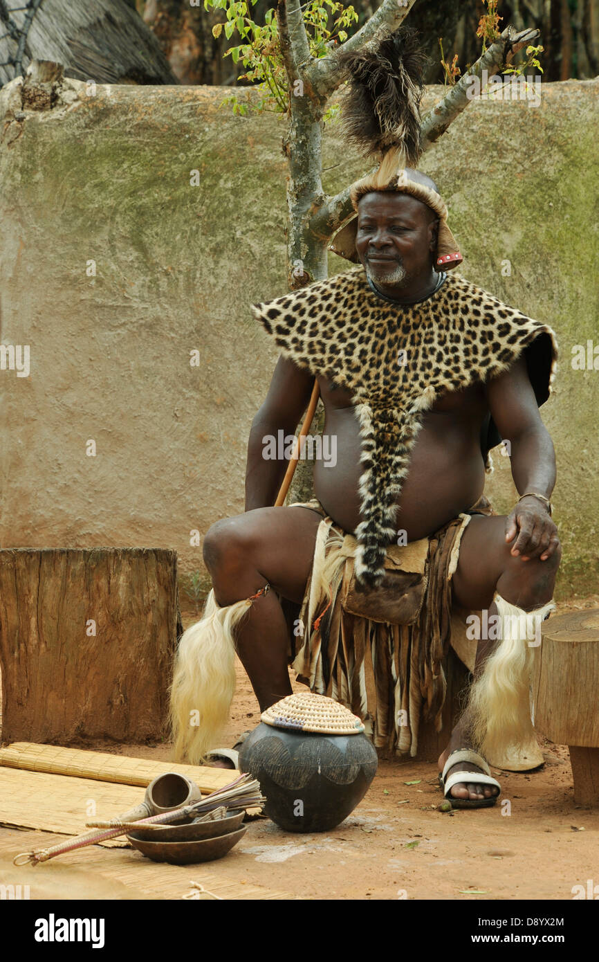 Zulu chief in ceremonial dress sitting next to pot of traditional Stock