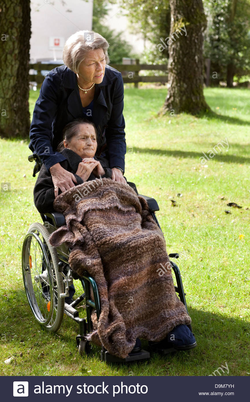 Daughter pushing her old disabled mother on a wheelchair in a garden