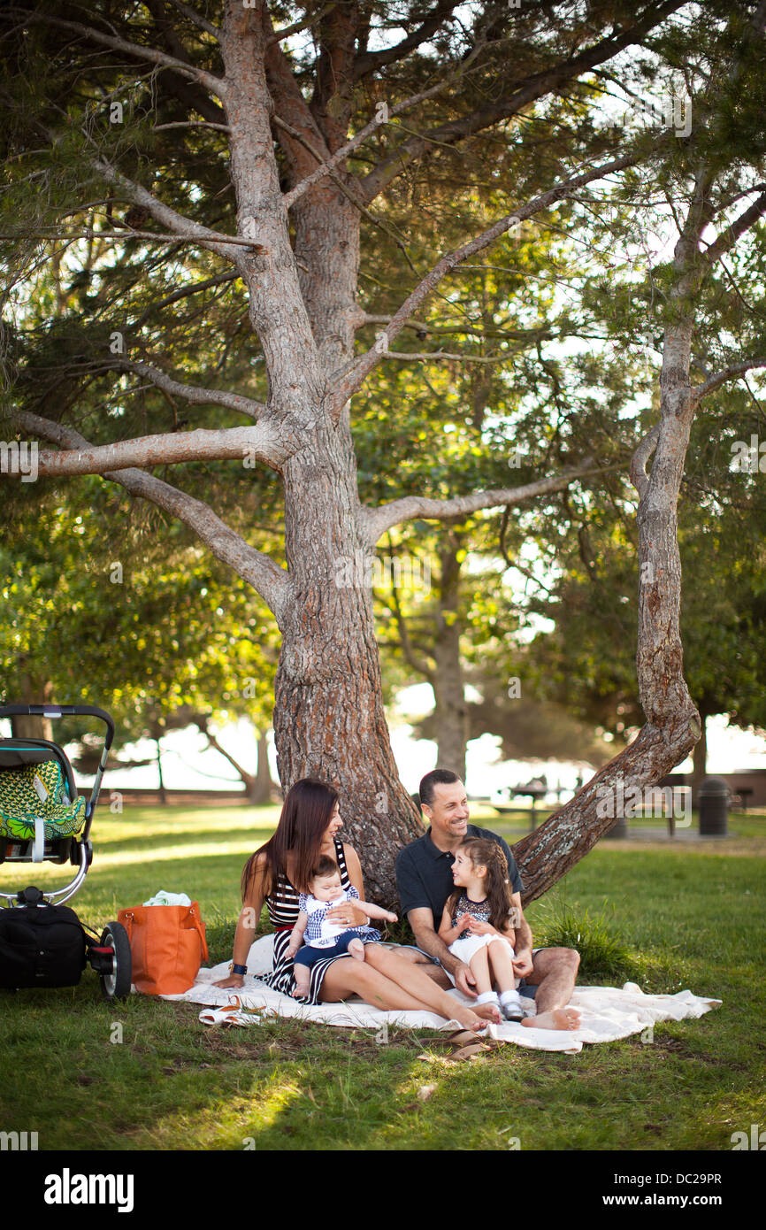 Family with two children sitting on picnic blanket under tree Stock