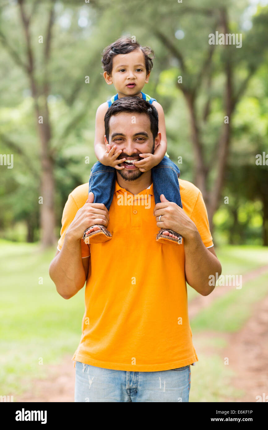 cheerful Indian father carrying son on his shoulders in the park Stock