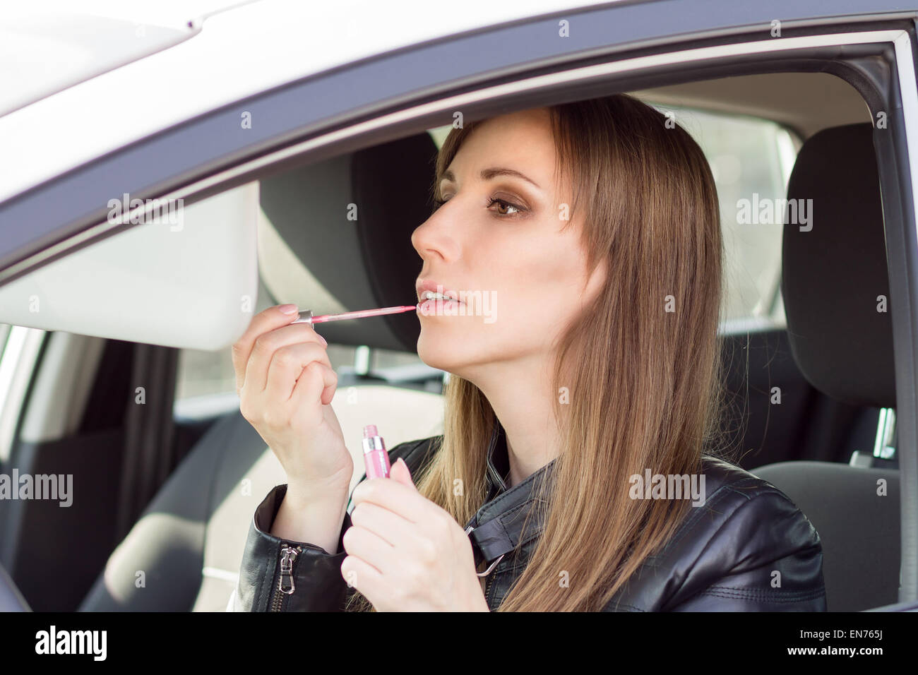 Young pretty woman apply makeup in car. Businesswoman with lipstick