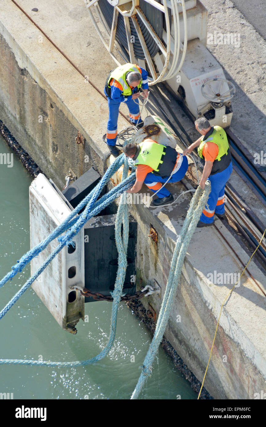 Three dock hands manhandling heavy wet mooring ropes to secure big