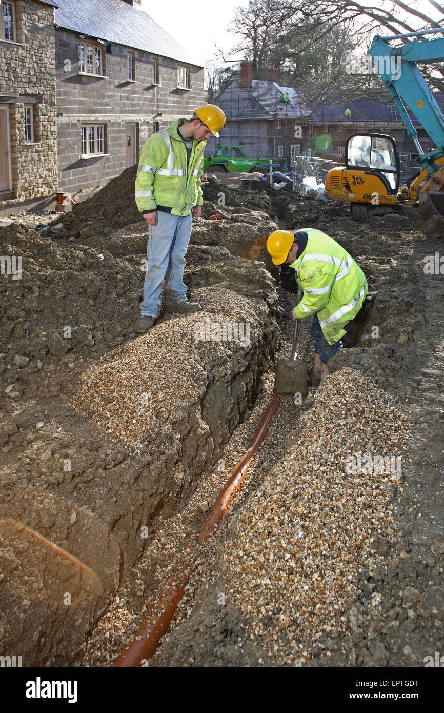 Construction workers install plastic underground drainage pipes on a