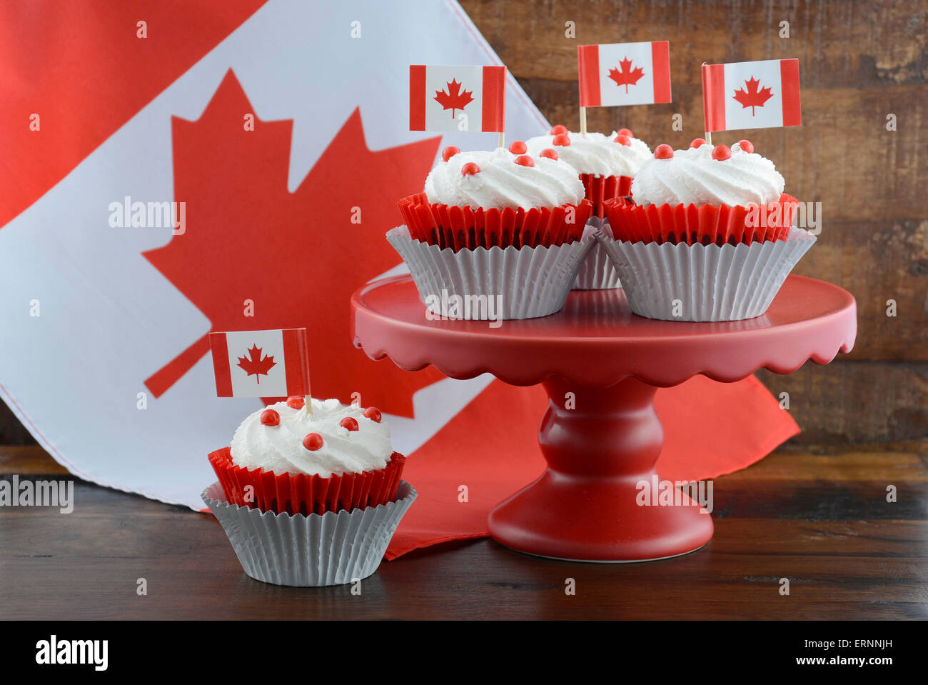 Happy Canada Day Celebration Cupcakes On Red Cake Stand With And White Maple Leaf Flag Against A Rustic Distressed Wood Back Happy Canada Day Celebration Cupcakes On Red Cake Stand With And White Maple Leaf Flag Against A Rustic Distressed Wood Back