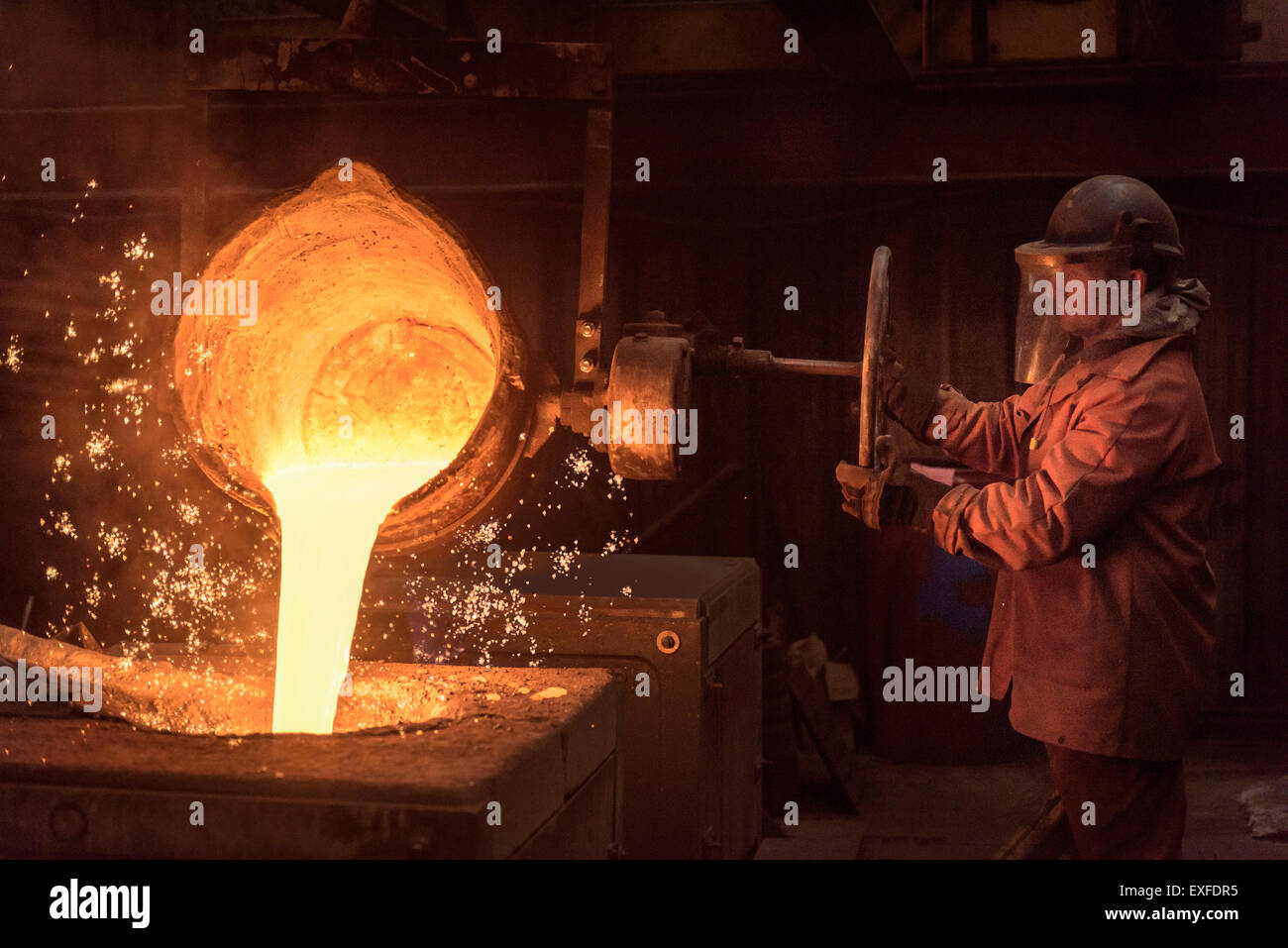 Worker pouring molten metal from flask in foundry Stock Photo