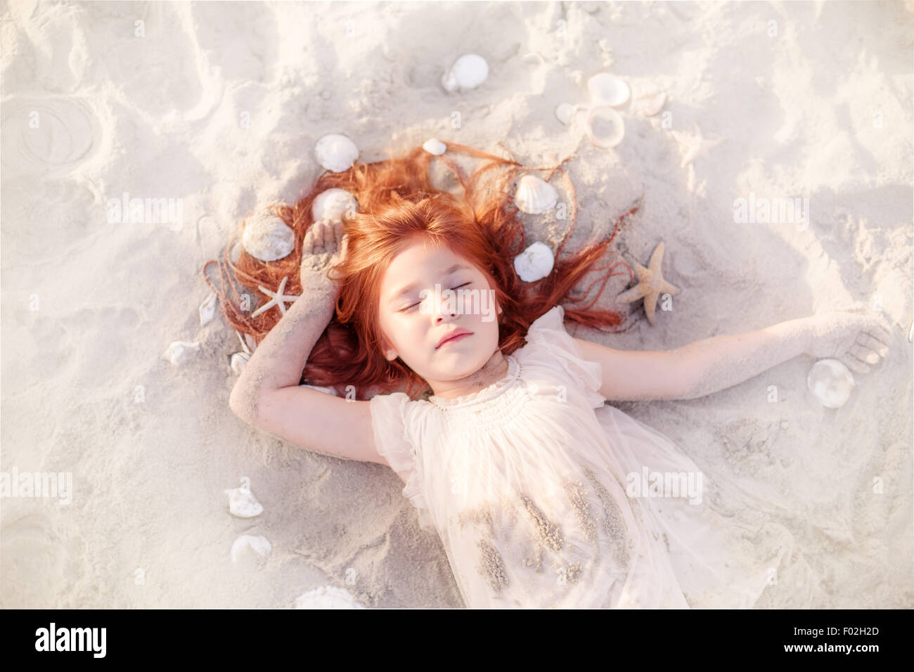 Girl sleeping on the beach with seashells in her hair Stock Photo