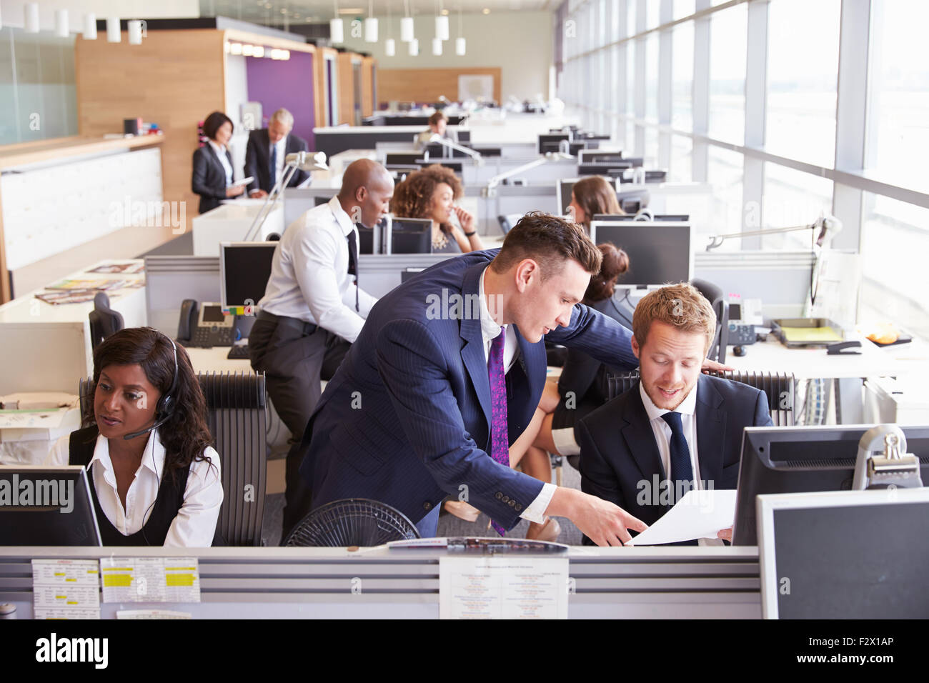 Two Businessmen Discussing Work In A Busy Open Plan Office Two Businessmen Discussing Work In A Busy Open Plan Office