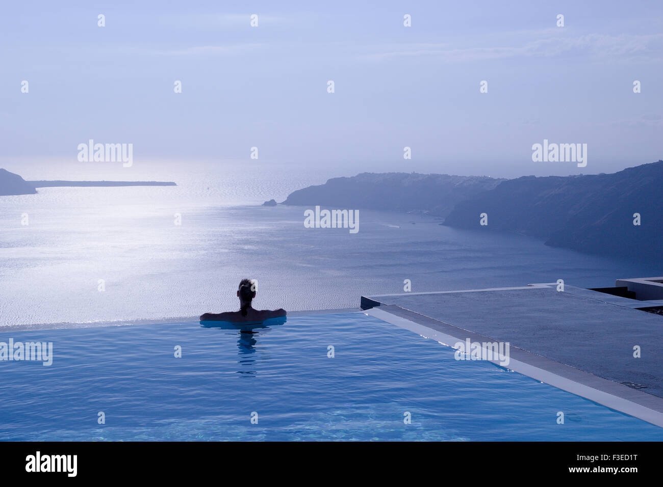 Female Silhouette In Infinity Pool On Cliff Edge Looking Out Over Blue Sea Santorini Greece Islands Female Silhouette In Infinity Pool On Cliff Edge Looking Out Over Blue Sea Santorini Greece Islands