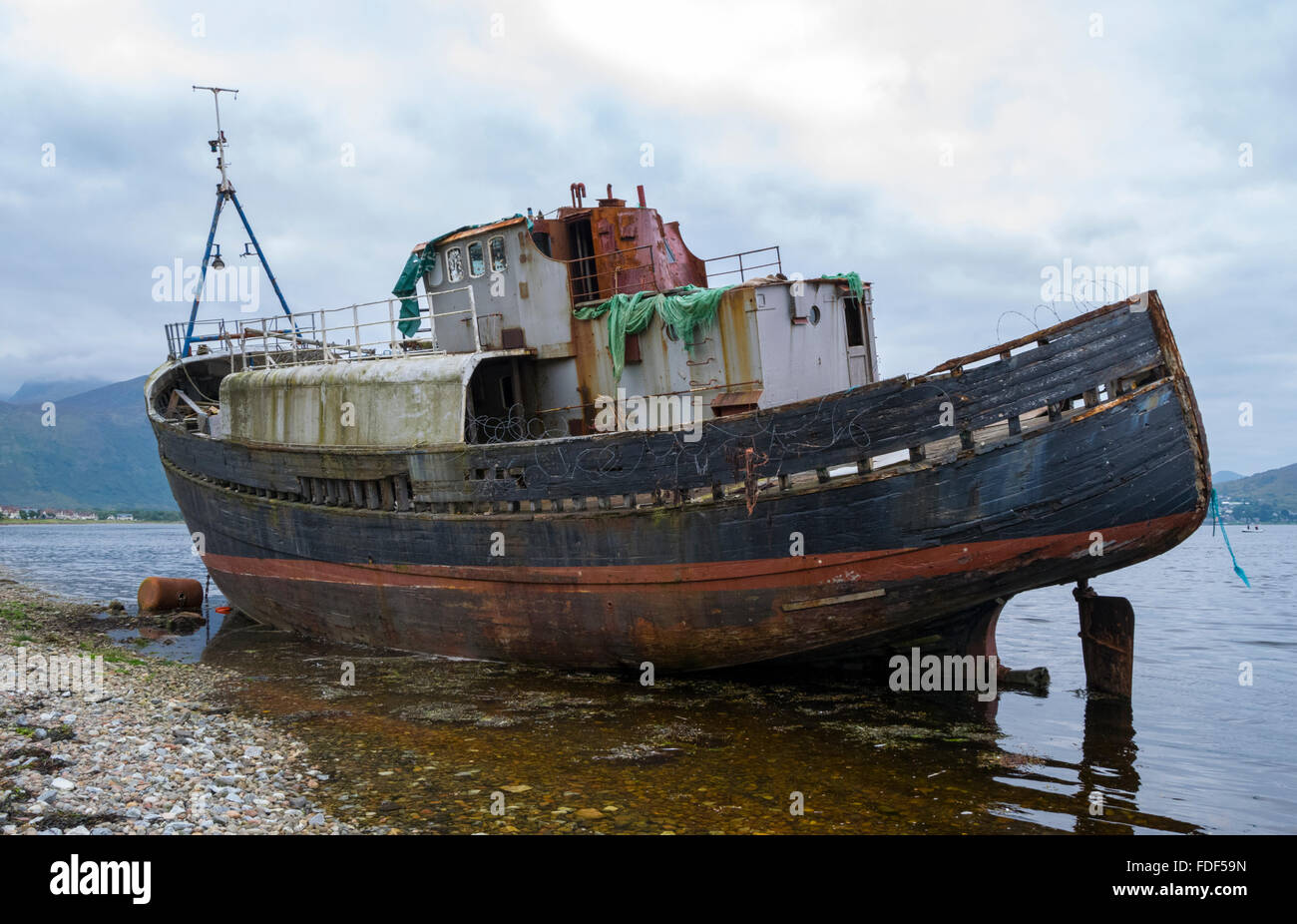 a-grounded-fishing-boat-on-a-beach-at-loch-linnhe-with-ben-nevis-in-FDF59N.jpg