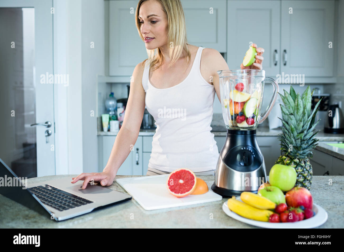 Pretty Blonde Woman Preparing A Smoothie With Recipe On Laptop Stock