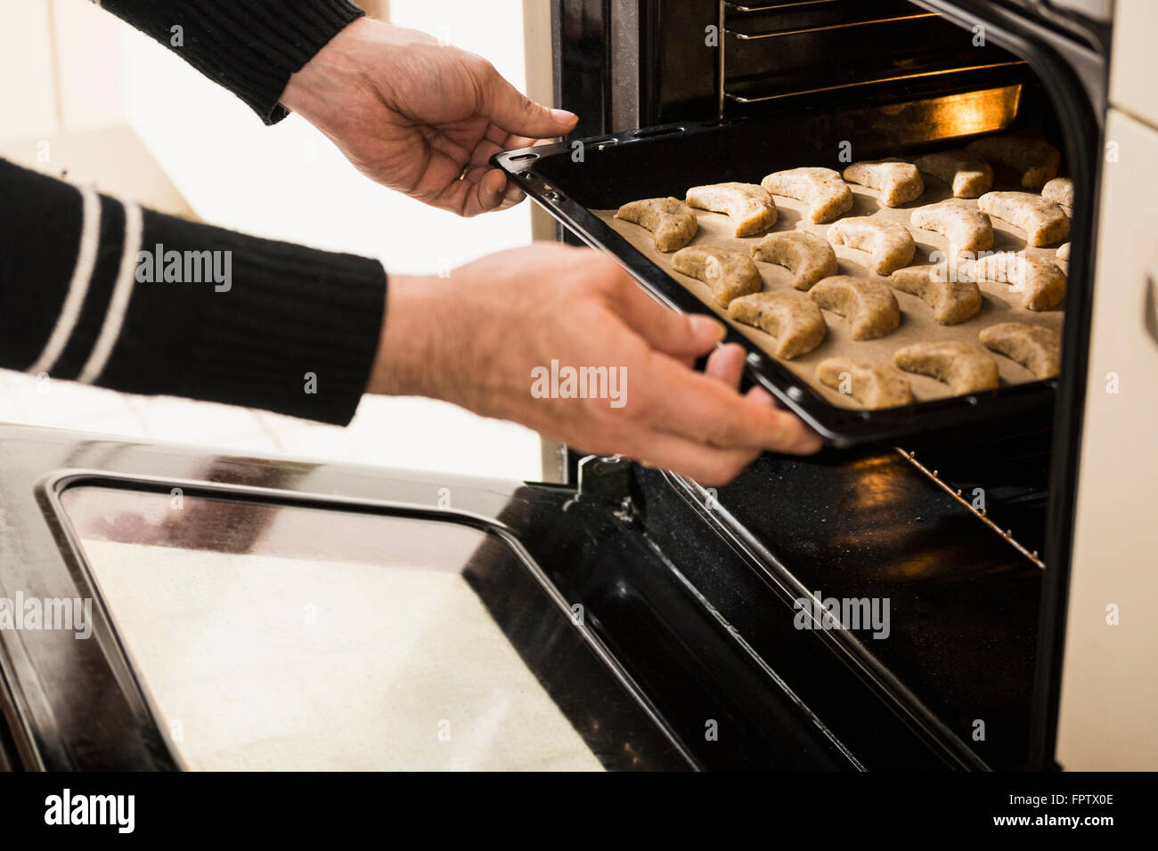Closeup of a man putting baking tray of vanilla crescents in oven