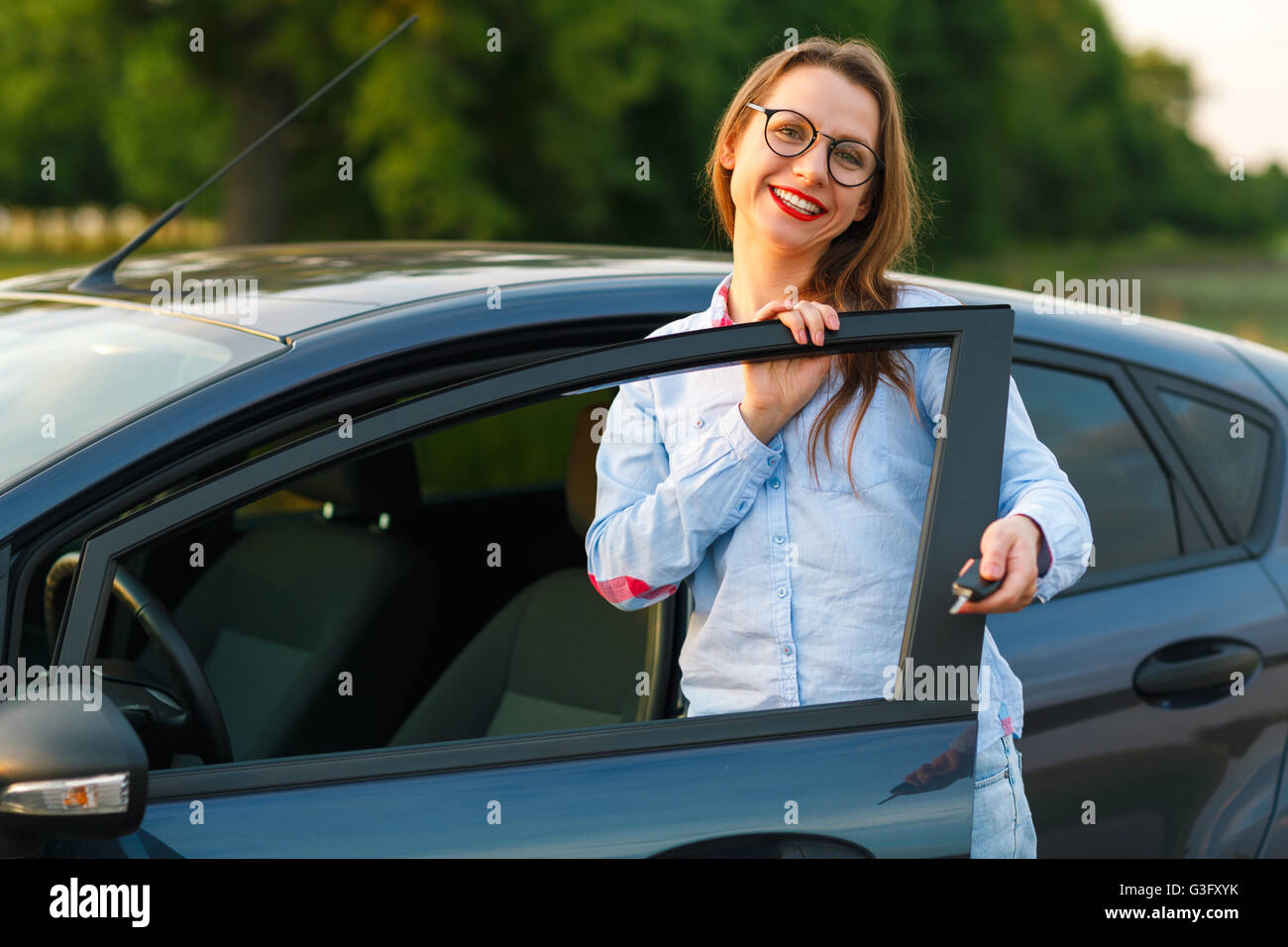 Young woman standing near a car with keys in hand concept of buying