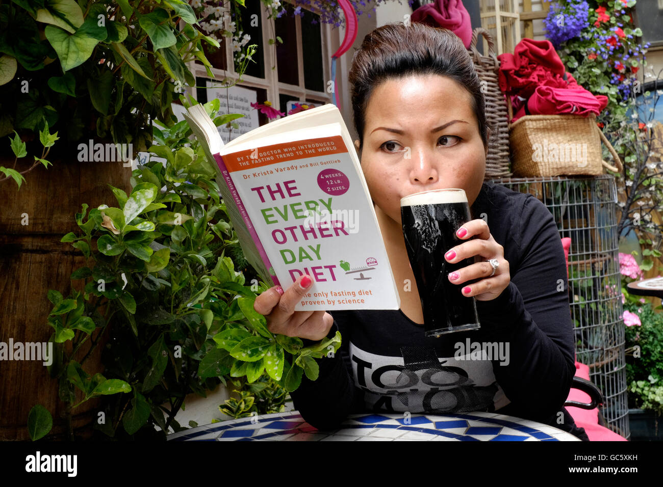 young-female-reading-dieting-book-while-drinking-beer-in-a-pub-garden-GC5XKH.jpg