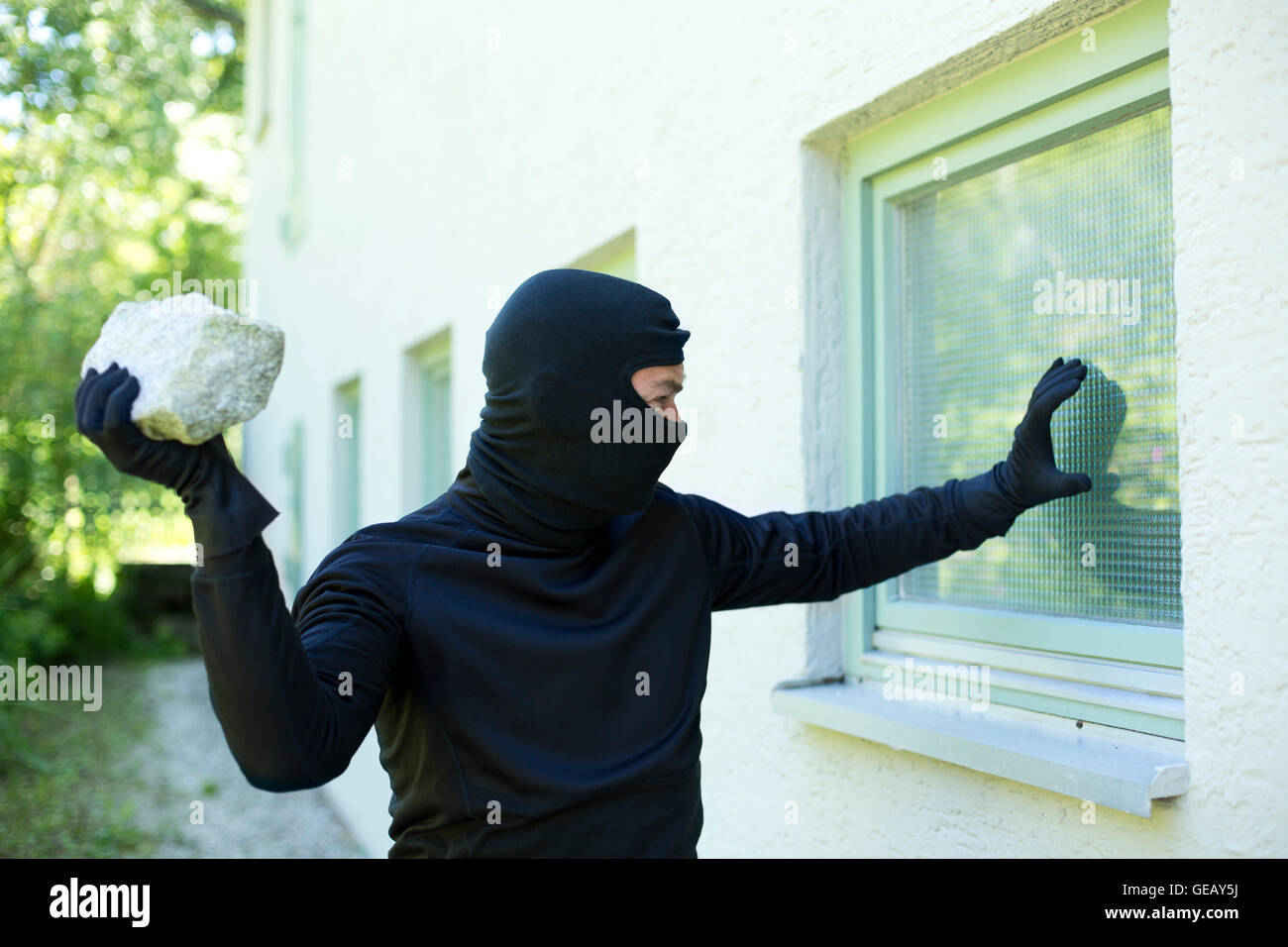 Burglar with stone breaking window Stock Photo, Royalty Free Image