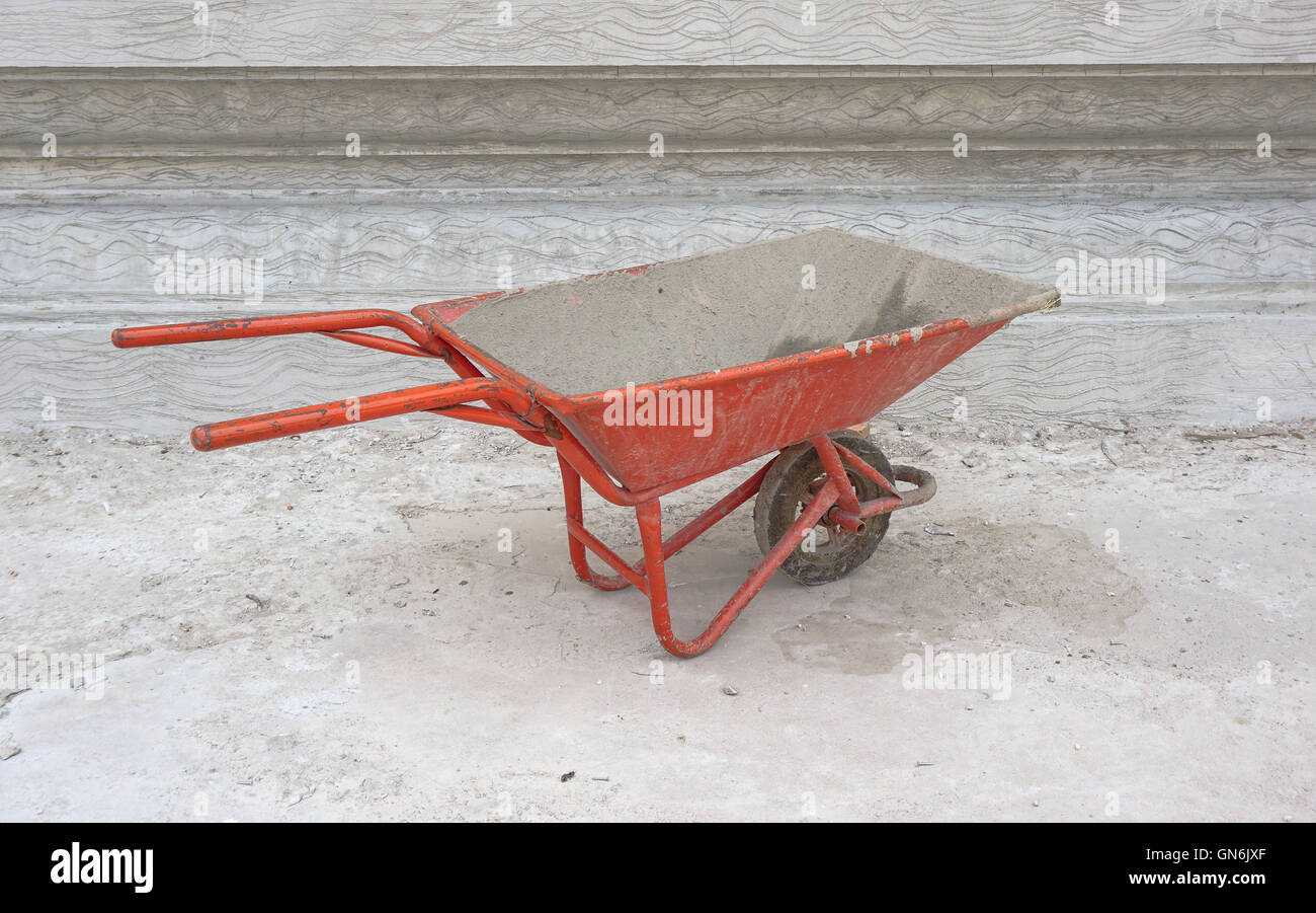Dirty cement wheelbarrow cart at construction site with unfinished