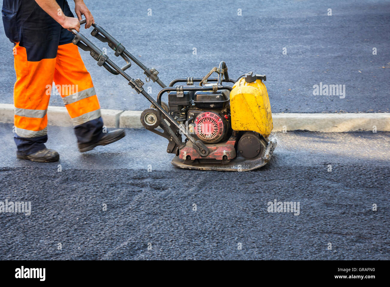 Worker use vibratory plate compactor compacting asphalt at road Stock