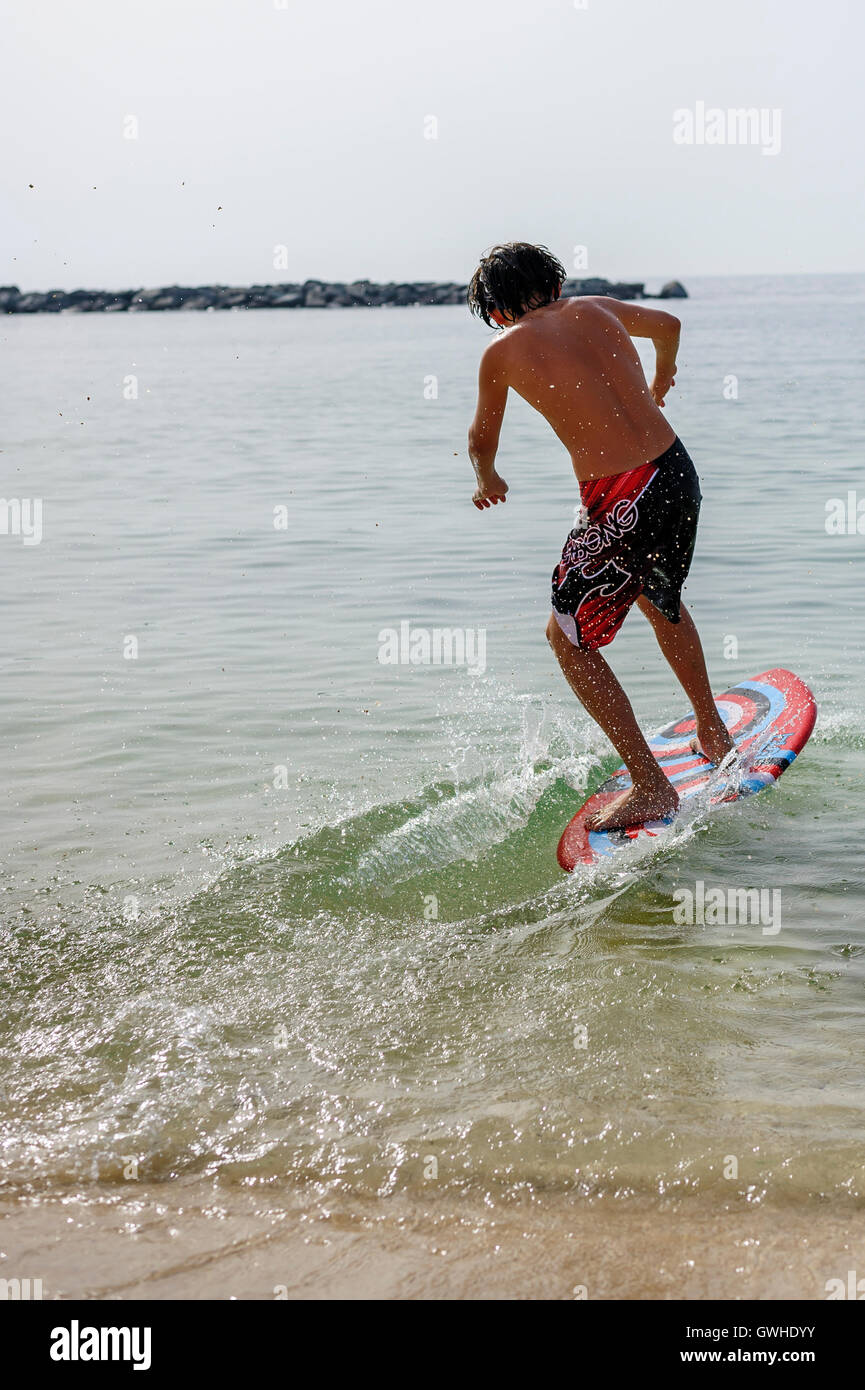 Teen (young boy) surfing with his skim board at the beach, Dubai Stock