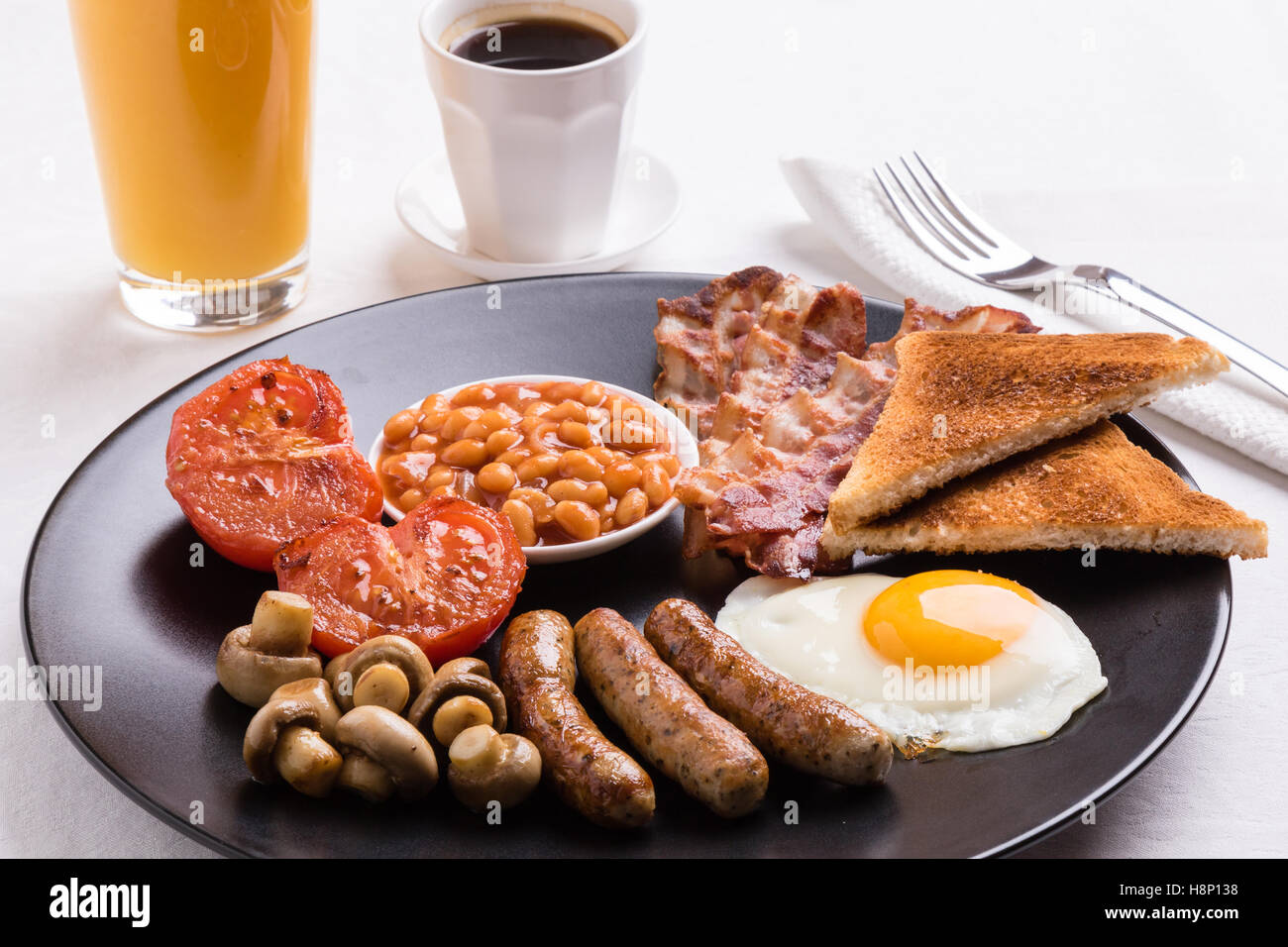full english breakfast with bacon, sausage, eggs, beans, mushrooms on