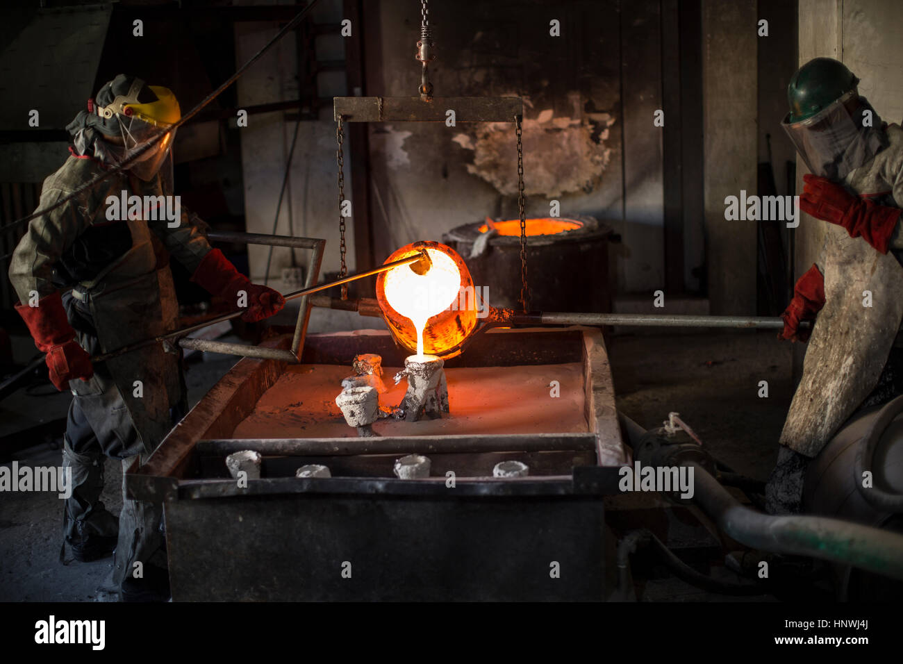 Metalworkers working in foundry, pouring molten bronze Stock Photo