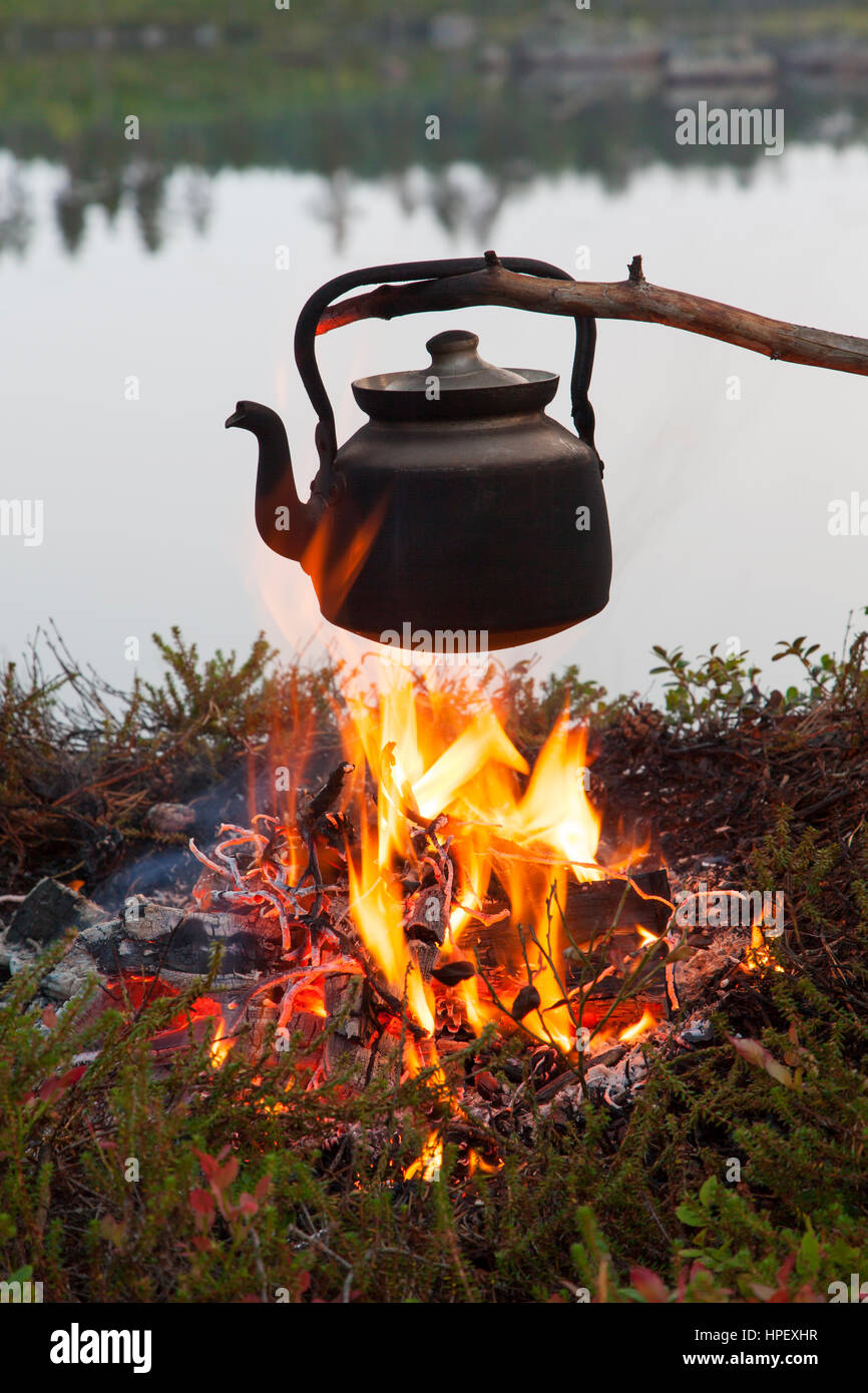 Blackened tin kettle boiling water over flames from campfire during