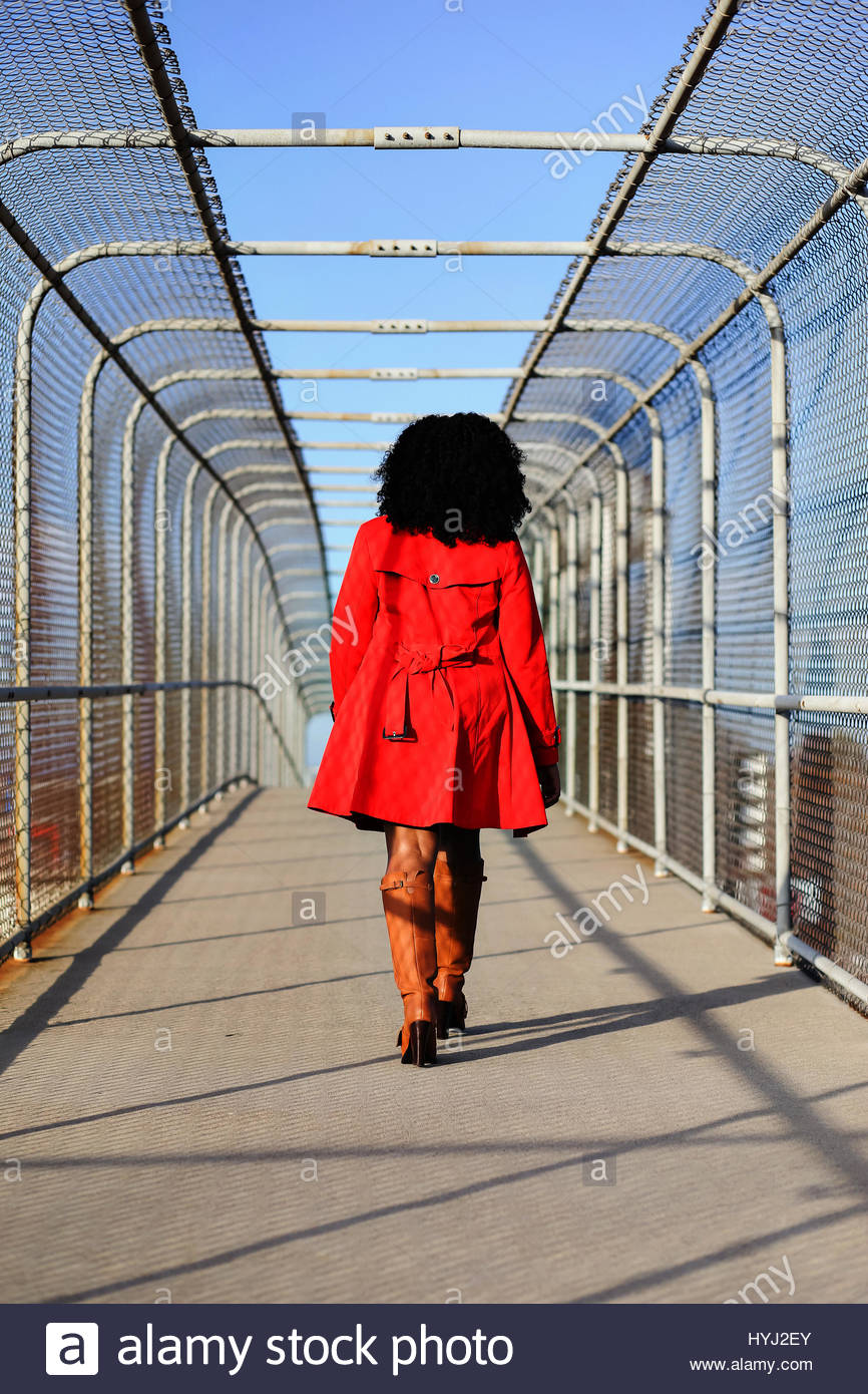 Young woman in a red coat walking away on bridge Stock Photo ...