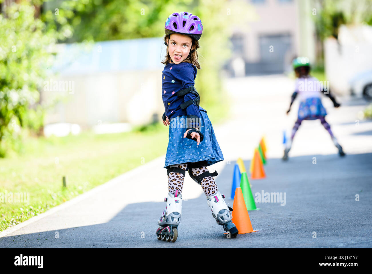 Children learning to roller skate on the road with cones. Twin girls