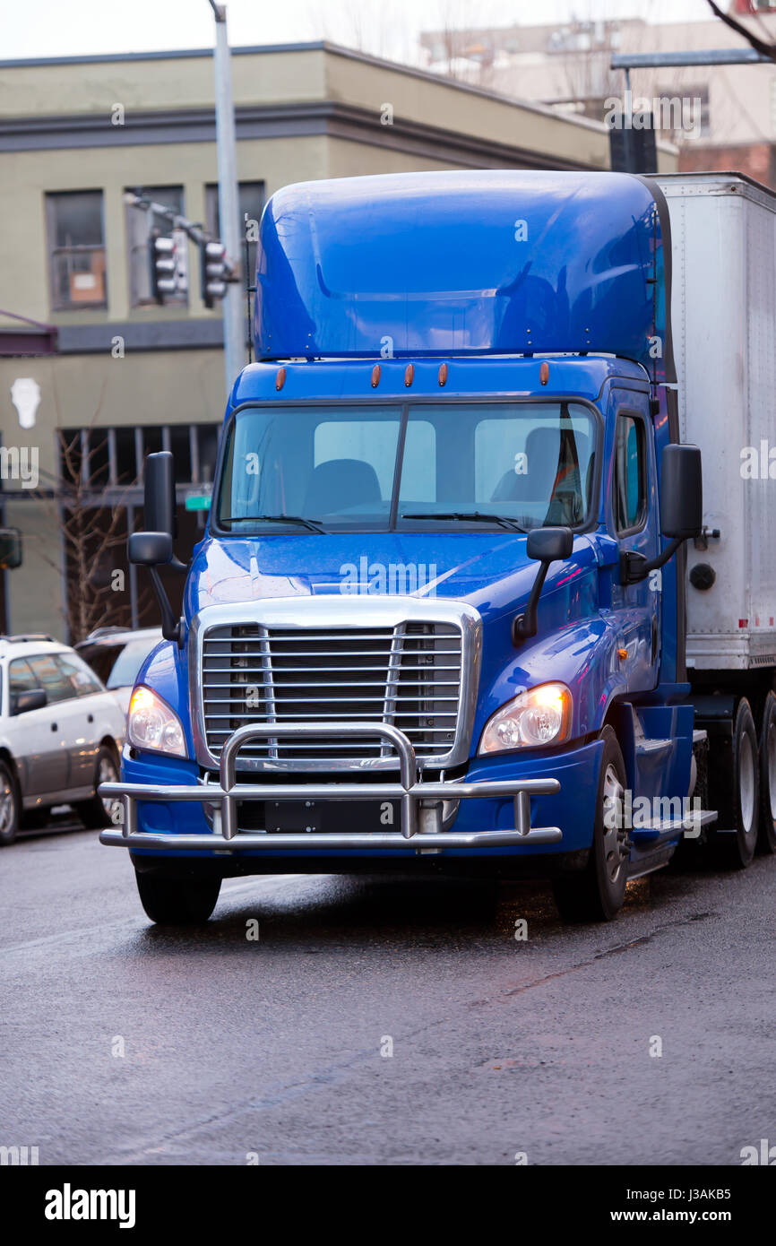 Bright modern big rig blue day cab semi truck with roof spoiler and