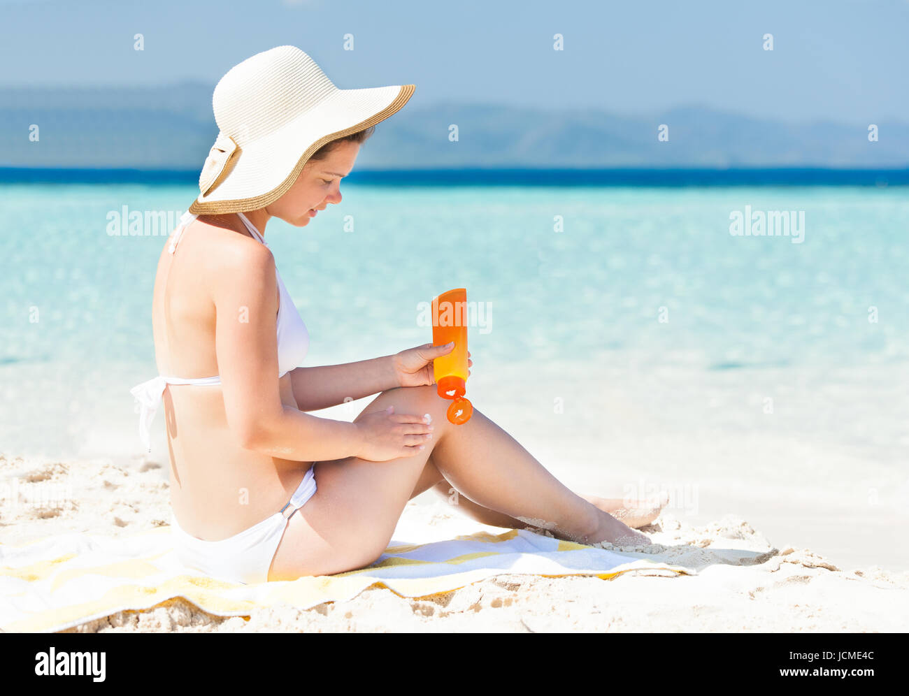 Side View Of Woman In Bikini Applying Sunscreen While Sitting On Beach