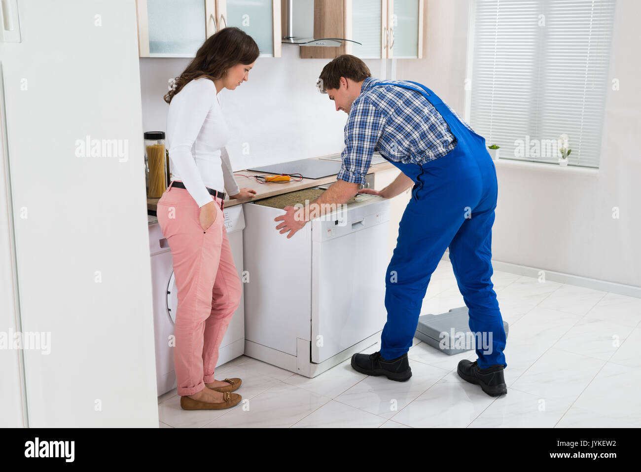 Male Worker Repairing Dishwasher While Woman Standing In Kitchen Male Worker Repairing Dishwasher While Woman Standing In Kitchen